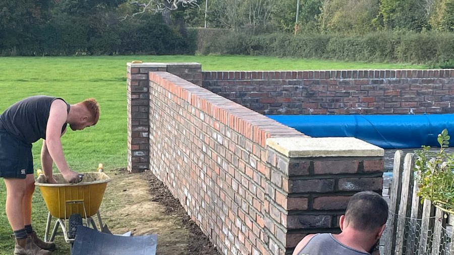 The Flint Landscaping team building a brick wall around a new swimming pool